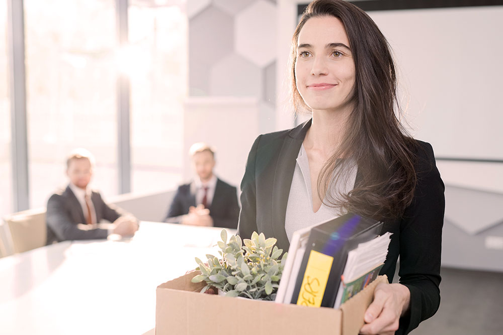 a woman with a glad expression leaves her job while holding a box